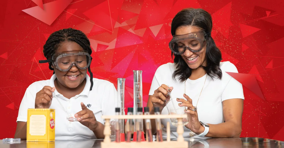 Une élève souriante et une mentore adulte portent des lunettes de protection et réalisent ensemble une expérience scientifique. Elles manipulent des béchers et des tubes à essai sur une table de laboratoire, avec un arrière-plan rouge vif à motifs géométriques. Toutes deux semblent engagées et enthousiastes.